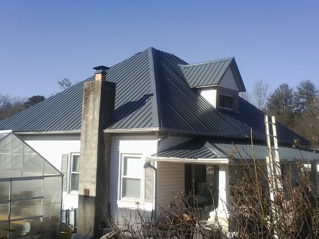 Dark blue standing seam metal roof on a white farmhouse with dormer — Slate & Tile Roof Repair by Roofing Brothers in Skippers