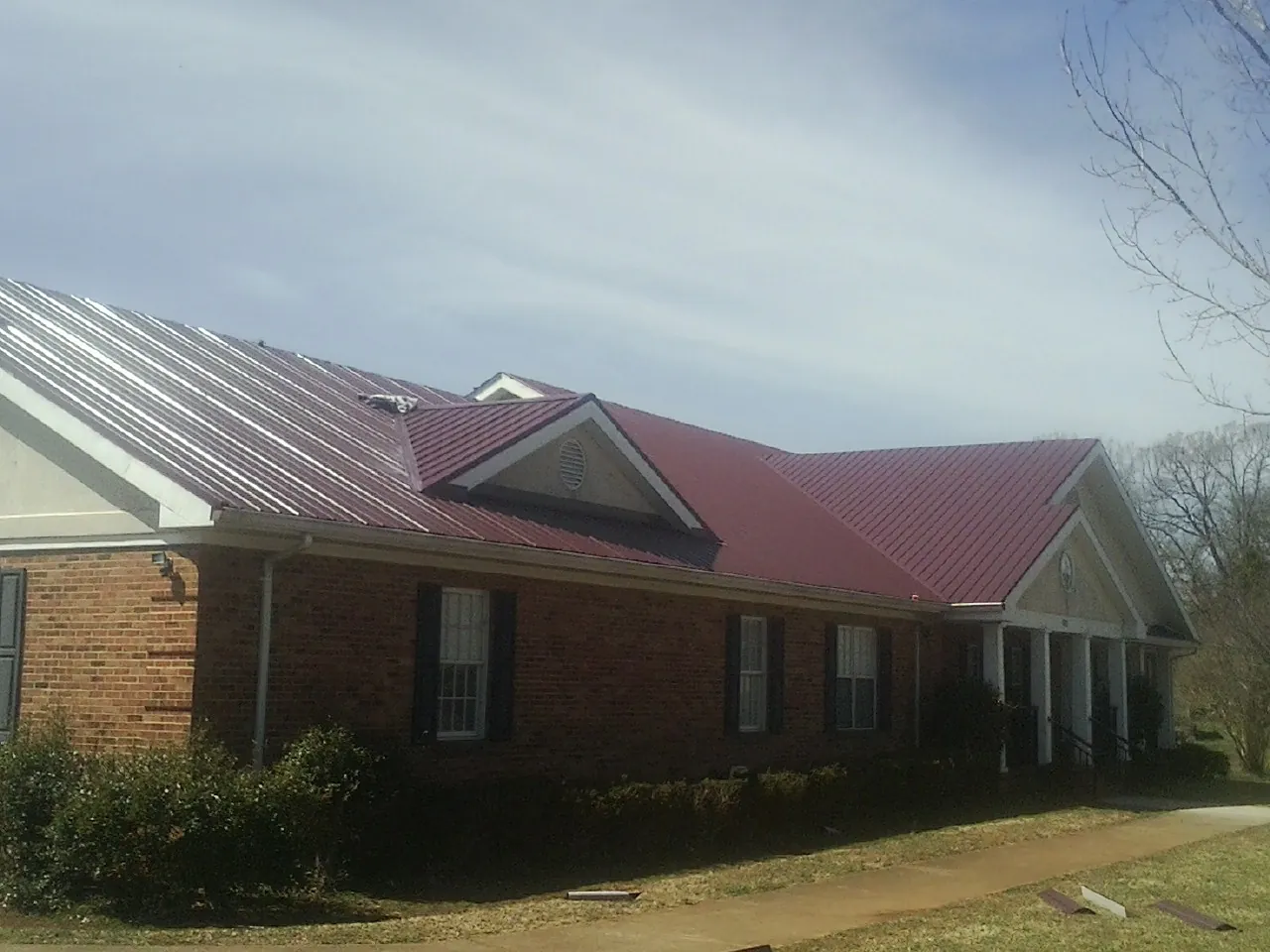 Red metal roof with gabled entries on a long brick building, from a Hail Damage Roof Repair job in Skippers