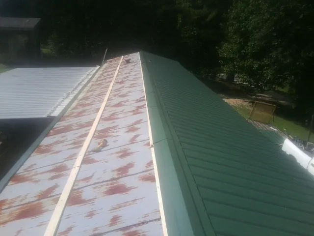 Old rusted panels beside newly installed green metal roofing — Wind Damage Roof Repair by Roofing Brothers in Skippers