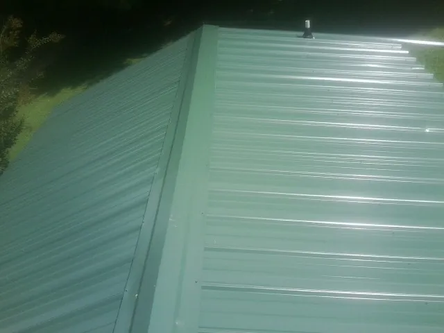 New green metal panels meeting at the ridge of a roof — Flat Roof Repair work by our crew in Skippers