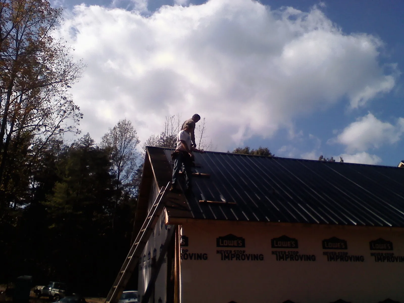 Roofer fastening dark metal panels high against a cloudy sky, from a Roof Inspection job in Skippers