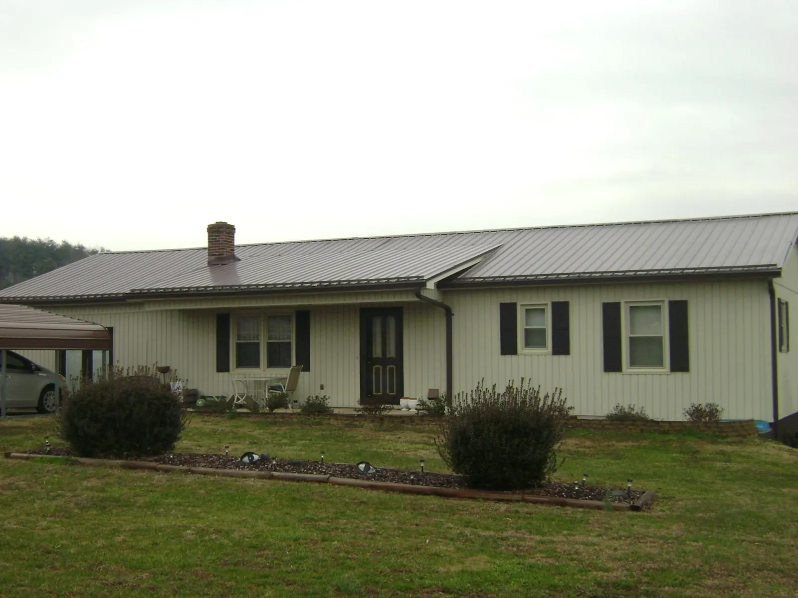 Brown metal roof on a cream sided ranch home with a brick chimney in Skippers