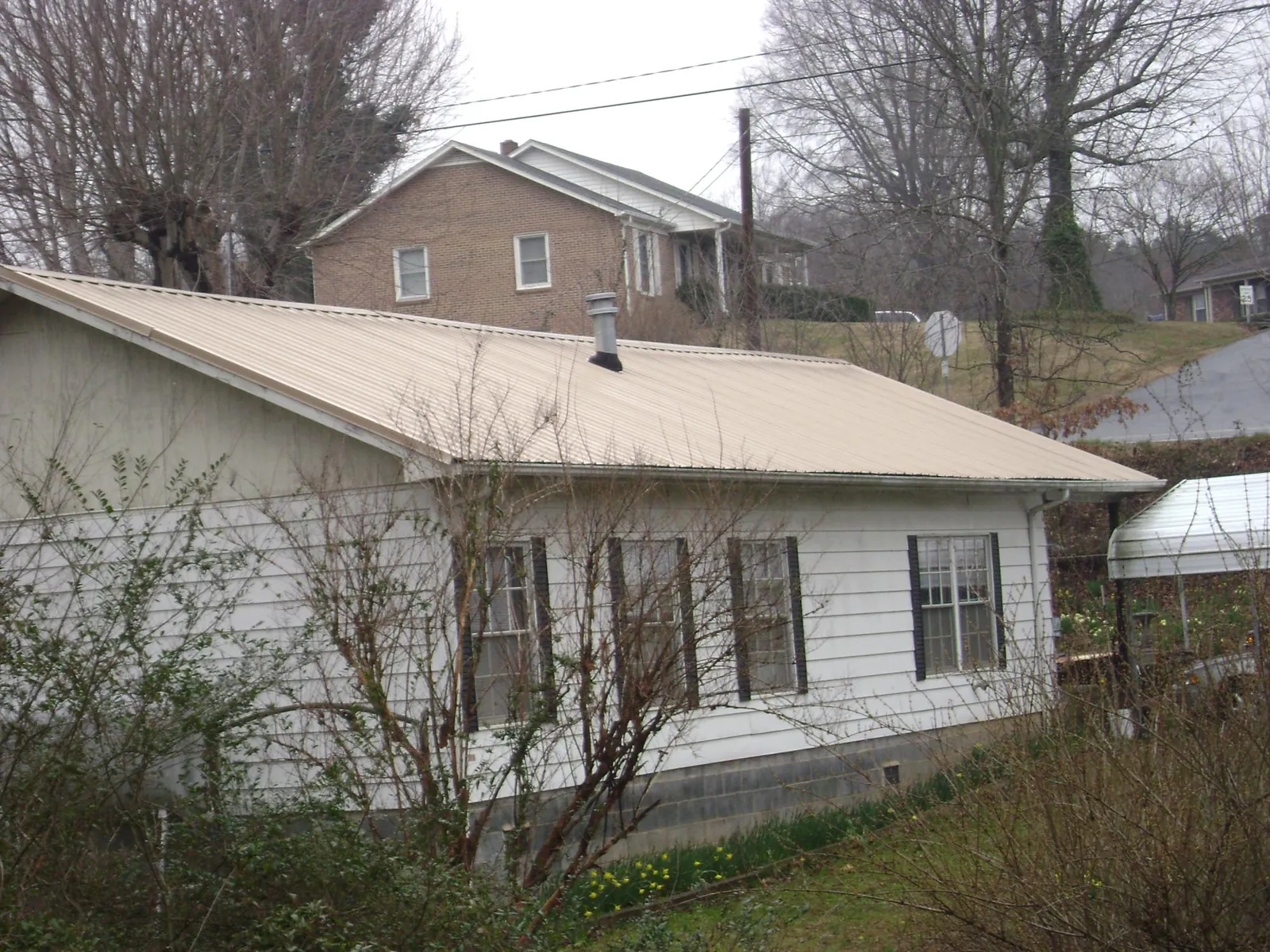 Tan metal roof on a white sided house set into a hillside — Commercial Roofing by Roofing Brothers in Skippers