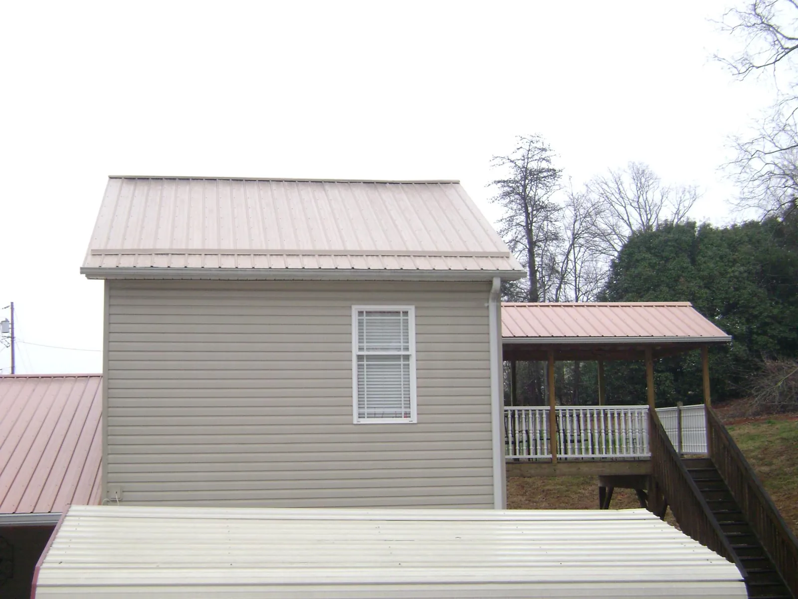 Tan metal roofs on a two story addition and attached porch, from a Roof Replacement job in Skippers